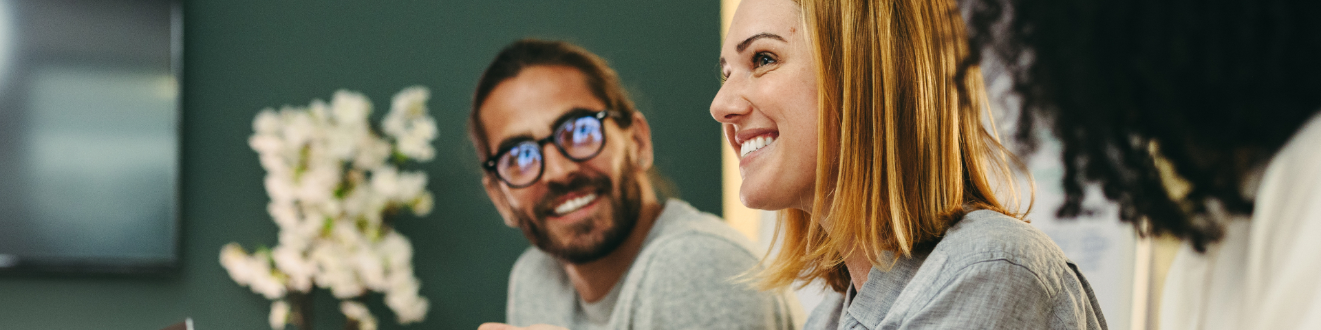Homens e mulheres sorrindo durante uma reunião de trabalho, demonstrando ambiente profissional e colaborativo.