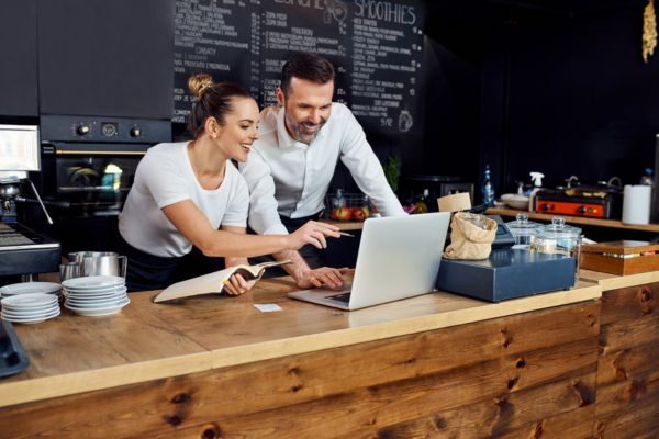 Cafés e restaurants em clima colaborativo com um casal trabalhando juntos em um laptop em um ambiente aconchegante e moderno. Eles mostram entusiasmo e trabalho em equipe.